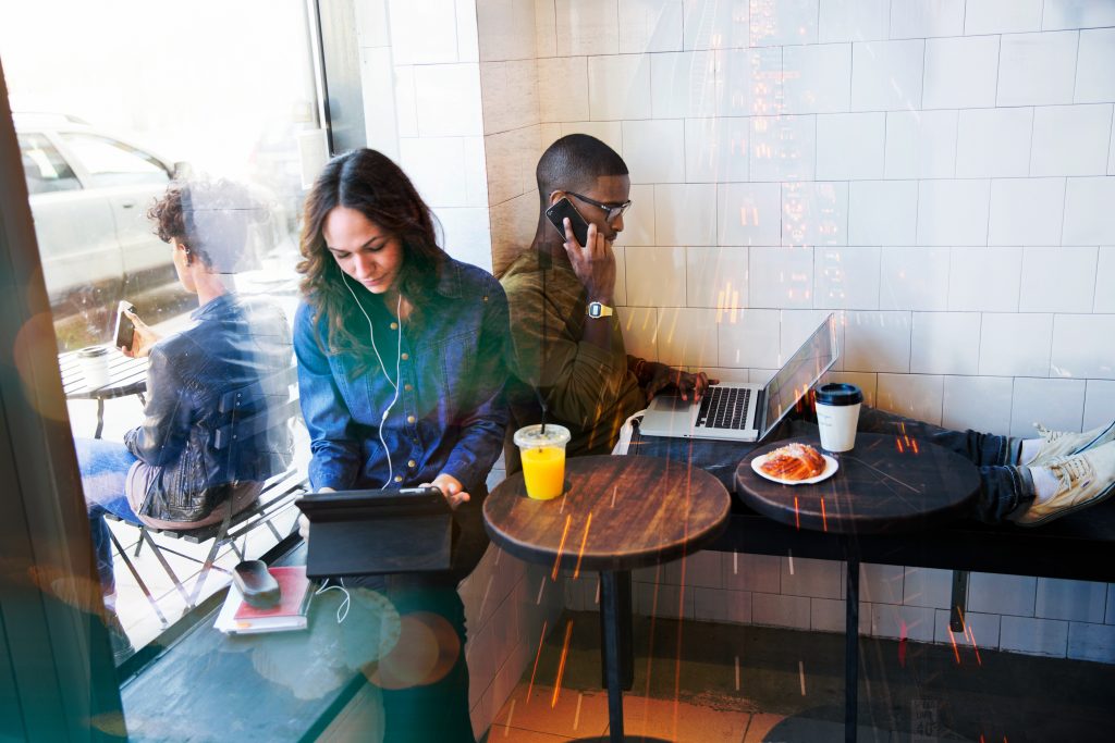 Kvinna och man sitter på ett café och jobbar med surfplatta och laptop framför sig