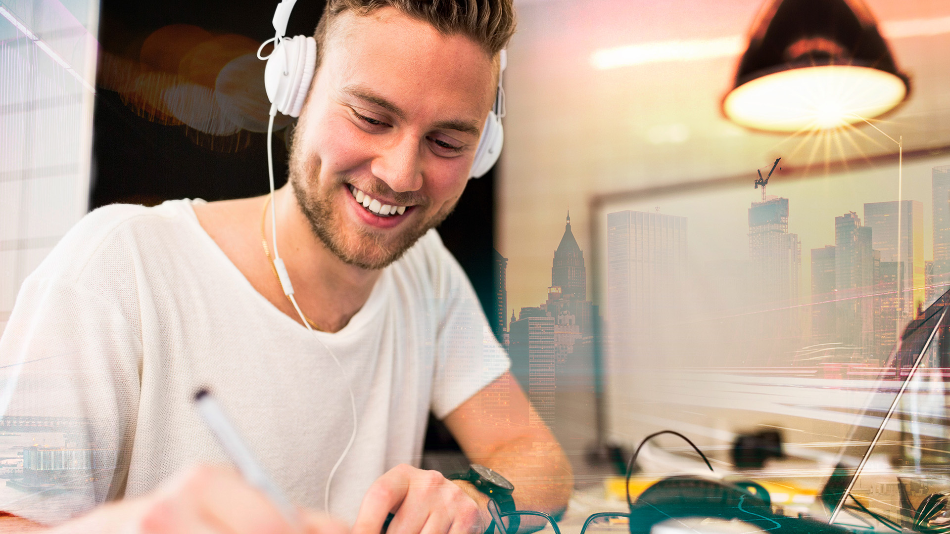 En leende kille med hörlurar på sig sitter i en cafémiljö och skriver.