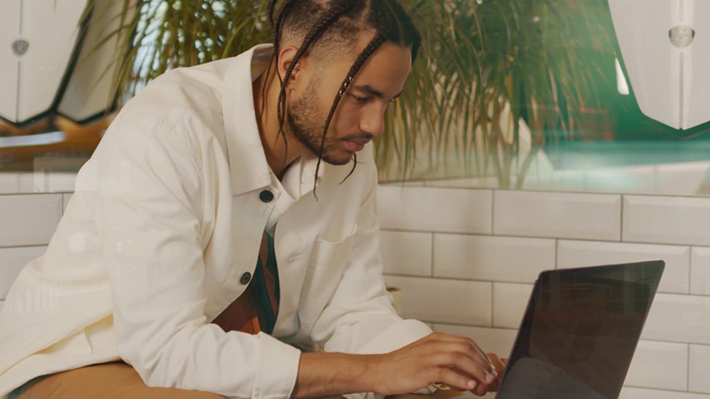 Man med vit skjorta fotad i profil som sitter och skriver på en laptop