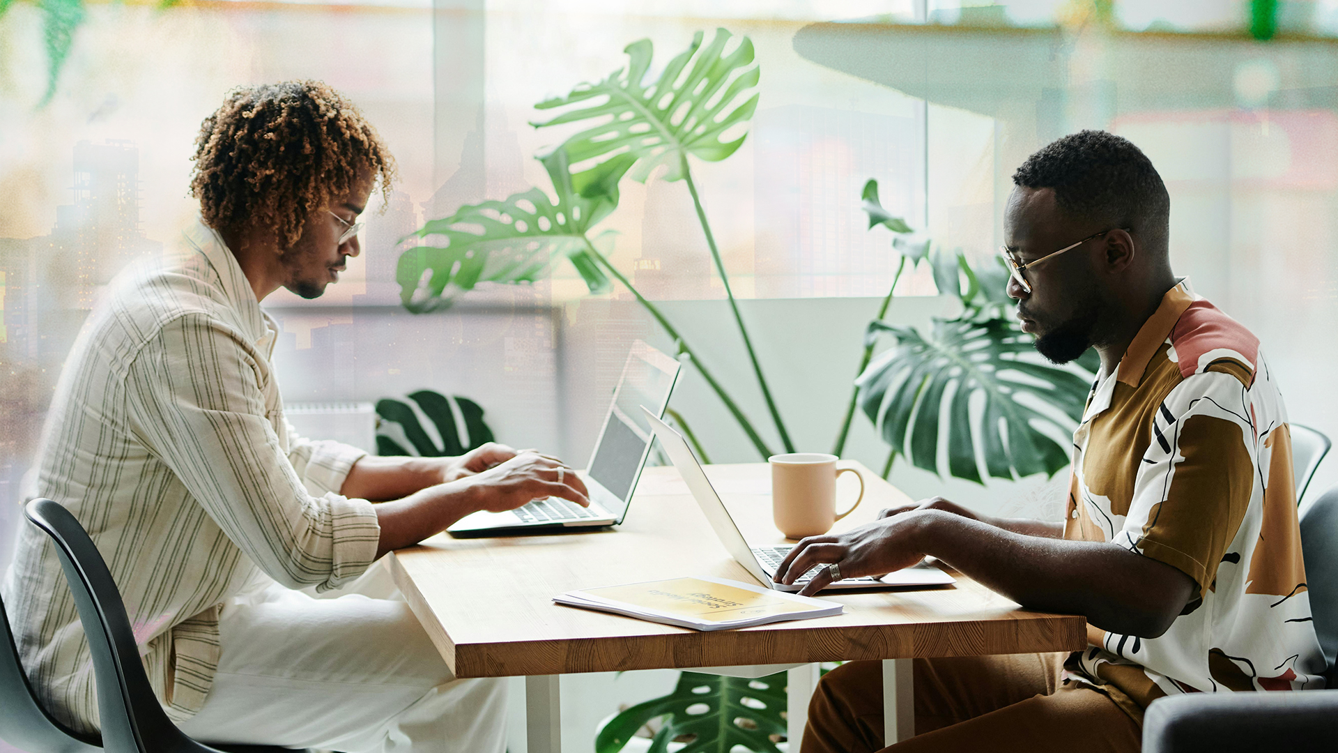 Två män som sitter vid ett kontorsbord och skriver på sina laptops